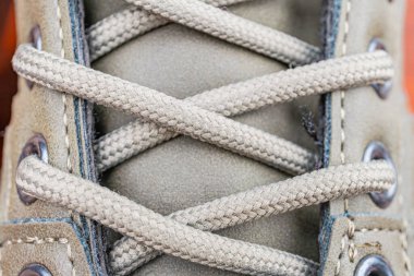 Beyaz ya da krem rengi, pruvada örülmüş ayakkabı danteli, muhtemelen açık hava ortamında, ayakkabı bağcığı kancası ile kolayca ulaşılabilir.