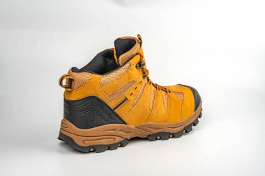 Açık gri arka planda, sağlam yapı ve ayak bileği destekli engebeli arazi için tasarlanmış yüksek tepeli bir yürüyüş botunun görüntüsü kahverengi, siyah ve sarı veya turuncu aksanlı Lik 'i içerir.