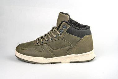 Üst kısmı koyu yeşil, üst kısmı koyu renkli, bronzlaşmış dikişler, beyaz kauçuk tabanlar ve beyaz arka planda sergilenen eşsiz dantel kapaklı bir spor ayakkabı.