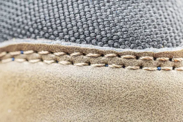 Lüks ayakkabı yapma detaylarını ön plana çıkaran yakın plan fotoğraf, bulanık bir arka plana karşı ayakkabıya dikişler vurgulanıyor.