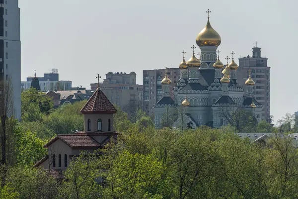Renkli bir şehir manzarası iki zıt binayı gösteriyor. Kırmızı kiremitli, kemerli bir bina. Muhtemelen solda bir kilise ya da belediye binası ve özenle hazırlanmış bir saray yapısı.