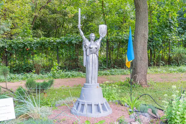 Muzaffer bir kadın heykeli, iyi korunmuş çimenler ve ağaçlarla çevrili bir bahçe ya da parktaki bir heykelin üzerinde duruyor. Ana Ukrayna ya da Özgürlük Heykeli - Kyiv, Ukrayna 06-11-2024.