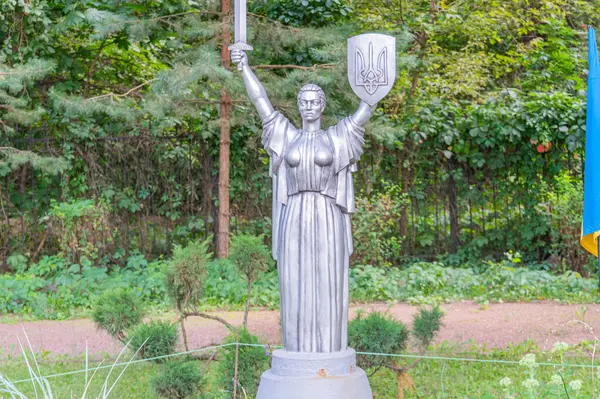 Muzaffer bir kadın heykeli, iyi korunmuş çimenler ve ağaçlarla çevrili bir bahçe ya da parktaki bir heykelin üzerinde duruyor. Ana Ukrayna ya da Özgürlük Heykeli - Kyiv, Ukrayna 06-11-2024.