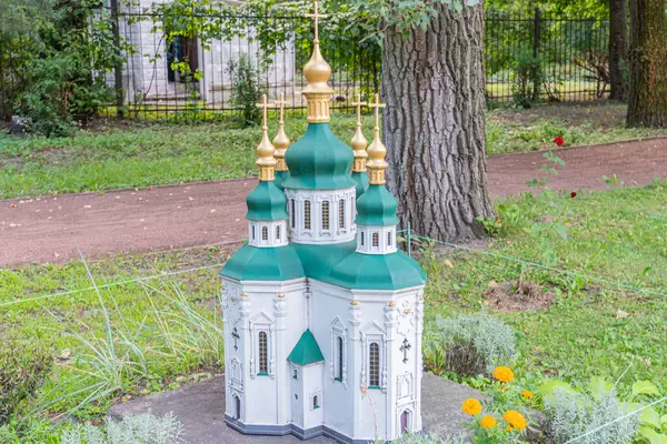 Çiçek açan bitkilerin arasında, soğan şekilli kubbeler ve altın yıldızlarla övünen minyatür bir Ukrayna kilise modeli bir park Kyiv, Ukrayna 06-11-2024 'ü işaret eden bir çit ve ağaçlarla çevrili.