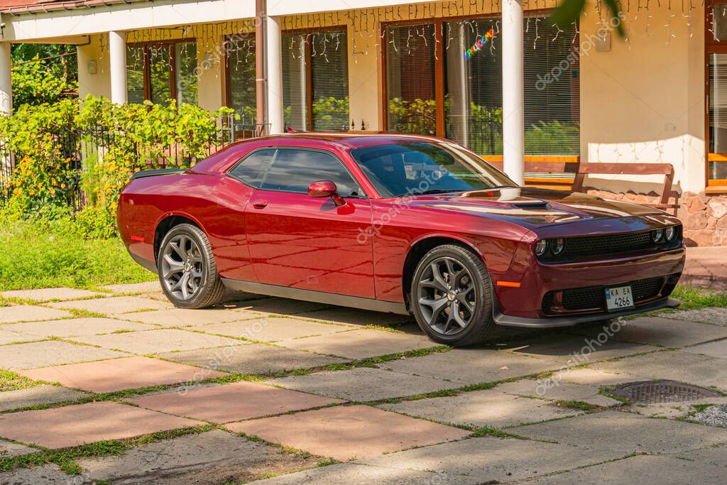 A close-up shot of a red Dodge Challenger, showcasing its muscular design and custom details, parked on a residential sidewalk from the mid-20th century Kyiv, Ukraine 06-11-2024