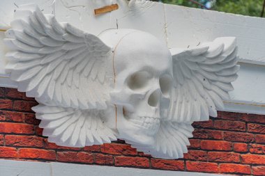Merkezinde, kuş tüyü benzeri elementlerle çevrili, sanat ve mimariyi harmanlayan bir resimde tuğla işçiliğine karşı kurulmuş, biçimlendirilmiş bir kafatası ile çarpıcı bir heykel rahatlaması. Pi Kyiv, Ukrayna 06-11-2024