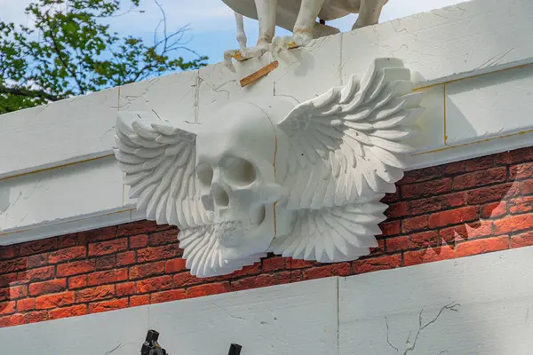 Görüntüde kanatlı bir kafatası heykeli sergiliyor, tuğladan bir yapıya entegre edilmiş, özgürlüğü simgeliyor veya kaçışı. Kafatası betondan ya da taştan yapılmış ve tasarım Kyiv, Ukrayna, 06-11-2024