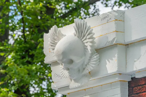 Resim, insan kafatası ve kuş kanatlarının yer aldığı dekoratif bir mimari heykel sergiliyor. Parça, çeşitli temalar ve Kyiv, Ukrayna 06-11-2024 ile harmanlanmış açık renkli taş bir yapıda sergileniyor.