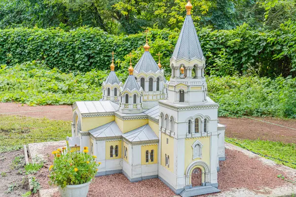 Birden fazla kubbe ve çapraz yapıya sahip minyatür Doğu Ortodoks kilise modeli, altın aksanlı beyaz cephelerle süslenmiş, yeşil zemin üzerine kurulmuş Kyiv, Ukrayna 06-11-2024
