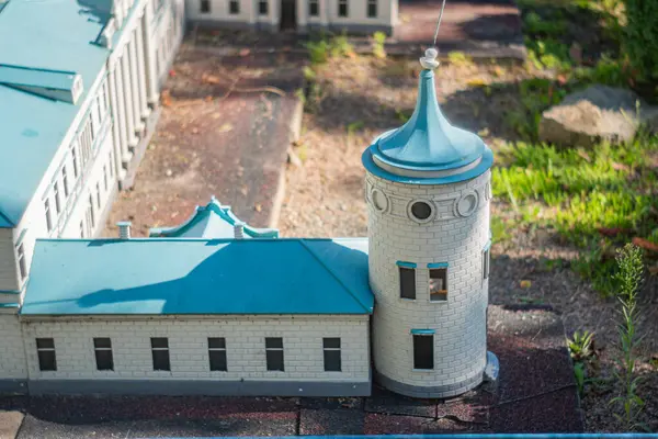 Çok katlı yapıya, simetrik pencerelere, potansiyel balkona, Akdeniz tasarımına, mavi kiremit çatısına, kuleye, Kyiv, Ukrayna 06-11-2024 noktalarına sahip minyatür bir taş bina.