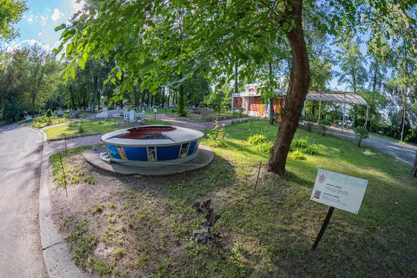 Doğa ve mimarinin bir karışımı ile sakin bir açık alan, büyük bir dairesel bitki, eski bir ahşap bina, gölge sağlayan ağaç, patika, işaret direği, ana Kyiv, Ukrayna 06-11-2024