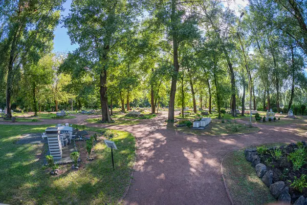 Görüntü, minimalist mimari, doğa ve simetriyi vurgulayan iyi korunmuş bir park veya mezarlığı gösteriyor. Yol, ağaçların altında durgun bir alana çıkıyor, har Kyiv, Ukrayna 06-11-2024