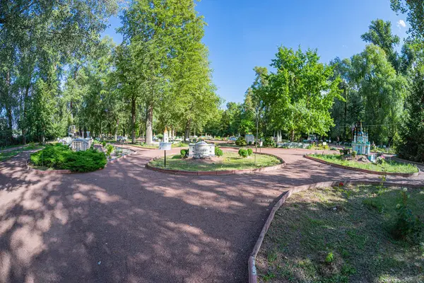 Doğanın ve mimarinin uyumlu bir karışımını sergileyen sakin bir şehir bahçesi, diğer bitkilerin arasında yalnız bir ağaca giden merkezi bir yola sahip tasarım Kyiv, Ukrayna 06-11-2024