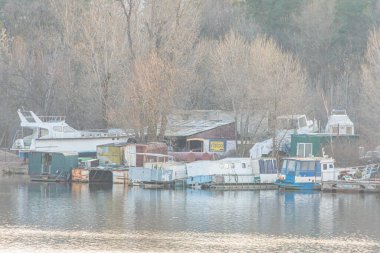 Rıhtıma yanaşmış teknelerin olduğu sakin bir marina sahnesi, muhtemelen uzun süreli olarak sakin bir su gökyüzünü yansıtıyor, sonbaharın sonlarında ya da kışın Kyiv, Ukrayna 'da, 03-29-2025