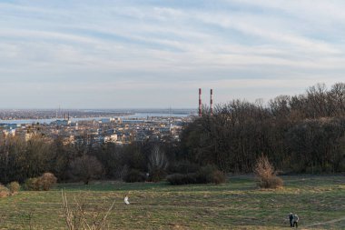 Panoramik bir görüntüde yemyeşil alanlar, eğlence faaliyetleri ve doğa ile kentsel yaşam arasındaki uyum gösteren bir şehir silueti yer alıyor: Kyiv, Ukrayna, 03-29-2025