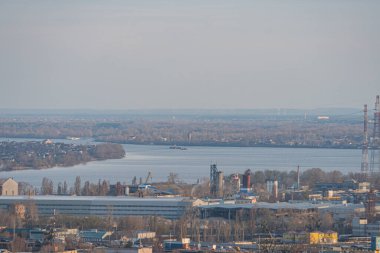 Birden fazla bina, endüstriyel yapılar ve su kütlesi yakınlarındaki inşaat alanlarının havadan görüntüsü. Bulutlu gökyüzü, u Kyiv, Ukrayna için uygun vinçler, 03-29-2025