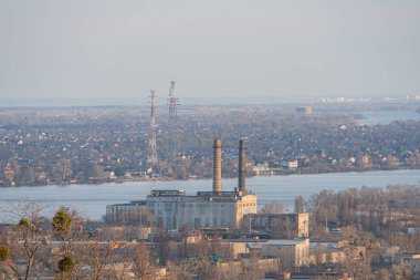 Bir su kütlesi yakınındaki endüstriyel kompleksin hava görüntüsü, önde gelen bacaları veya kuleleri ve yemyeşil çevresi Kyiv, Ukrayna, 03-29-2025 olan büyük bir tesisi gösteriyor.