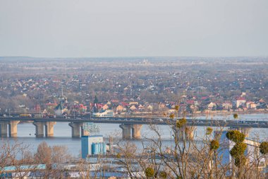 Bereketli yeşillik ve yakındaki kentsel altyapı Kyiv, Ukrayna, 03-29-2025 ile çevrili mavi bir su üzerinde köprüsü olan sakin bir manzaranın havadan görüntüsü.