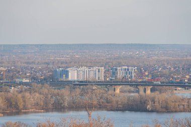 Şehrin ufuk çizgisine sahip sakin bir göl manzarası, kentsel bağlantı için bir köprü sergileniyor ve seyahat veya yaşam tarzı reklamı için ideal hava koşullarını yansıtıyor Kyiv, Ukrayna, 03-29-2025