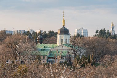 Panoramik bir manzarada altın kubbeleri ve yemyeşil çatıları arasında yer alan tarihi bir Rus katedrali, kültürel mirası ve çağdaş kentsel gelişimi simgeliyor: Kyiv, Ukrayna, 03-29-2025