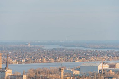 Konut, sanayi ve doğal alanların yer aldığı, fabrikalar veya elektrik santralleri Th Kyiv, Ukrayna, 03-29-2025 gibi çeşitli mimari ve potansiyel endüstrilerin sergilendiği manzaralı bir kıyı kasabası.