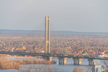 Kyiv, Ukrayna, 03-29-2025 gibi seyahat reklamları ve gayrimenkul reklamları için ideal yüksek görüş açısına sahip bir noktadan yakalanan, yansıtıcı bir su kütlesi üzerinde kablo destekli köprü gösteren panoramik bir görüntü.