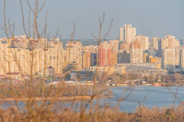 Gündoğumu veya günbatımında gökyüzü manzaralı, suların kenarındaki modern binaları yelkenli tekneler ve yansıtıcı sakin nehirle sergiliyor, Kyiv, Ukrayna, 03-29-2025 arasında sakinliği iletiyor.
