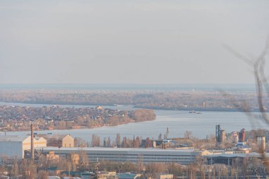 Endüstriyel bir rıhtım bölgesi, muhtemelen bir haliç ya da koy, fabrikalar ve vinçlerle, ticaret, gelişme ve potansiyel çevresel etkiyi yansıtan Kyiv, Ukrayna, 03-29-2025