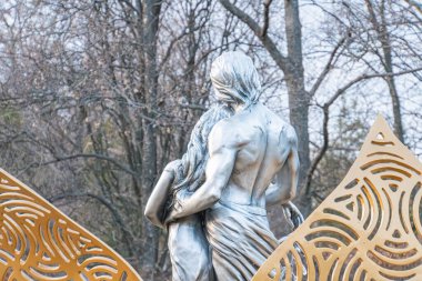 Modern bir sanat kurulumunda iki dinamik, karmaşık desenli metal figür bulunur. Bulutlu bir gökyüzü ve ağaçların altında yer alır. Kyiv, Ukrayna, 03-29-2025 'e göre birlik veya hareketi sembolize eder.