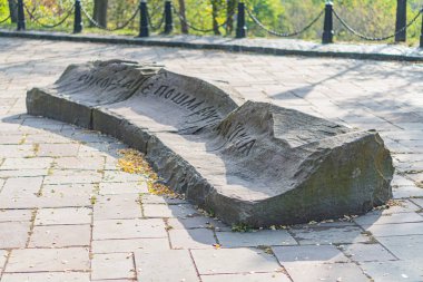 İnsan yapımı ve doğal elementlerin zıt olduğu sakin bir park ortamında engebeli bir taş bank, ziyaretçileri ağaçların arasında dinlenmeye davet ediyor.