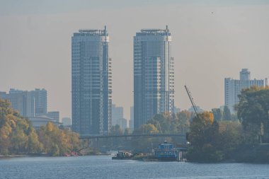 Şehir silüeti, yüksek cam gökdelenler, yemyeşil ağaçlar, insan yapımı ve doğal elementlerle tezat oluşturan sakin nehir, sahil yolu, tekne, sürdürülebilir şehir yaşamı.,