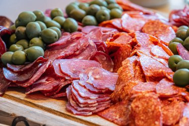 Sofrada ya da tezgahta, yumuşak doğal aydınlatma altında pişmiş et, salam, pepperoni ve zeytin karışımıyla dolu beyaz bir tabağın yakın çekimi.