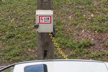 Açık hava sahnesinde yıpranmış bir parkmetre, yakındaki sarı bir elektrik uyarı levhası ile ahşap bir direğe bağlanmış sarı bir kablo tabelanın altındaki yere bağlanmış.