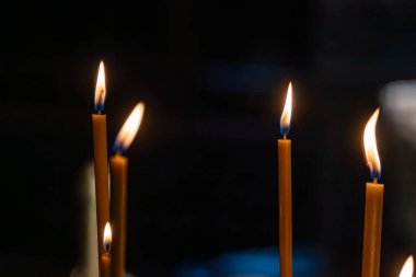 Yakından çekilmiş üç mum resmi kutsal bir ortamda, sıcak gölgeler bırakarak doğal ışıklandırma mum dokusu ve alev titreşimi ile gerçekçi bir tarzda