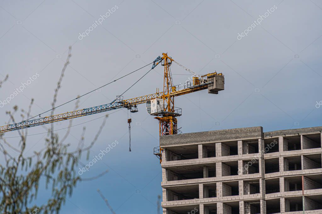 Overcast daylight image of a construction site with an extended yellow crane lifting metal structure, surrounded by various stages of building frames, made from concrete and rebar The perspective is