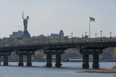Birçok kemerli bir köprü, doğanın ve kentsel manzaraların karışımına karşı kurulmuş bir nehir boyunca uzanır. Yapısı beton, sağlam ve simetrik olarak tasarlanmıştır. Surroun Kyiv, Ukrayna 04-17-2025