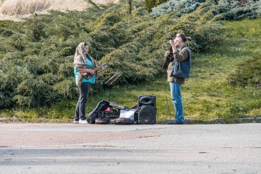Biri akustik gitar çalan iki kişinin açık hava müzik performansı ve diğeri de günlük ritim ayarları natura Kyiv, Ukrayna 04-19-2025 ile bir park veya kamusal alan öneriyor.