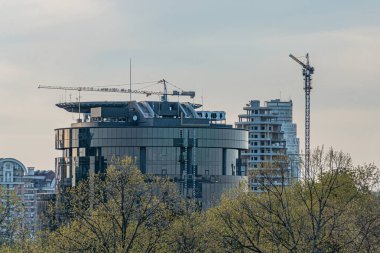 Alacakaranlık şehri uzun, çeşitli binalar, önemli inşaat vinçleri, iş bölgesi ayarı, derin blues ve griler, insan ya da hareket eden araçlar yok, Waterma Kyiv, Ukrayna 04-19-2025
