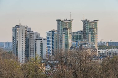 Çağdaş, yansıtıcı gökdelenlerle çevrili yoğun nüfuslu bir kentsel alanın yükselişinden görüntü yeşil bulutlu gri gökyüzü Kyiv, Ukrayna 04-19-2025