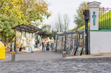 Sokak sahnesi kaldırım taşları, eski dünya cazibesi, kilise benzeri bina, açık tezgah, renkli posterler, sarı şemsiye tahtası, sonbahar ağaçları, yumuşak li Kyiv, Ukrayna 10-11-2024