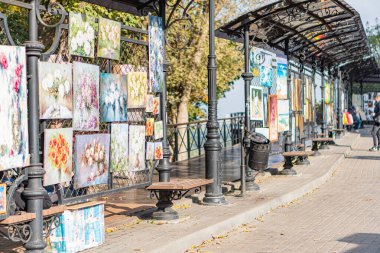 Yürüyüş boyunca uzanan açık hava sanat galerisinde, sıcak tonlarda canlı çiçek resimleri sergileniyor. Benches 'in yanında yürüyen iki kişi, şehir çevresi Kyiv' i, Ukrayna 10-11-2024 'ü davet ediyor.