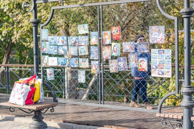 Bir kişi ahşap bir köprüde duruyor, elinde renkli sanat eserleri, yemyeşil yeşilliklere tepeden bakan manzara öğleden sonra Kyiv, Ukrayna 10-11-2024 'te bir parkta ya da doğa koruma alanında gibi görünüyor.