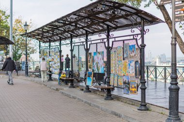 Tuğladan yapılmış kaldırım yolu, kafes çatılı metal sığınak, renkli posterler, küçük ahşap bank, yumuşak ışıklandırma, yeşil yapraklı ağaçlar, ca Kyiv, Ukrayna 10-11-2024