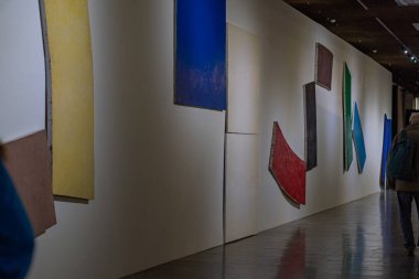 Modern soyut sanat galerisi geometrik resimleri canlı renklerde sergiliyor. Beyaz duvarlar, fayanslı döşemeler, koruyucu cam veya bariyer, yumuşak tepe lambası Kyiv, Ukrayna 10-20-2024