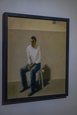 Gri arkaplan üzerine gerçekçi sanat eserlerinde sessiz renklerde oturan bir adam, muhtemelen bir yağlı boya ya da benzeri bir ortam, yumuşak gölgeler ve nötr ifade Kyiv, Ukrayna 10-20-2024