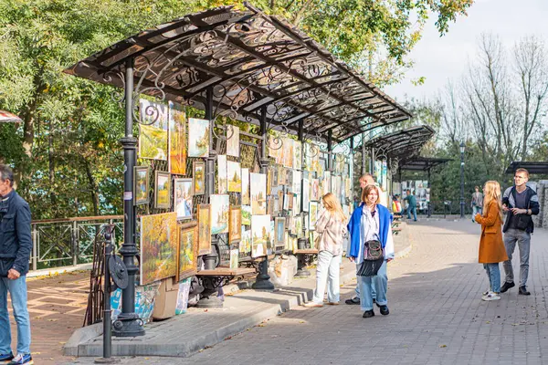 Şehir manzarası, hareketli sokak, renkli tabloları koruyan büyük şemsiye derme çatma galeri ya da açık hava tezgahı, tuğla kaldırım, insanlar yürüyor, dinamik unsur, temiz Kyiv, Ukrayna 10-11-2024
