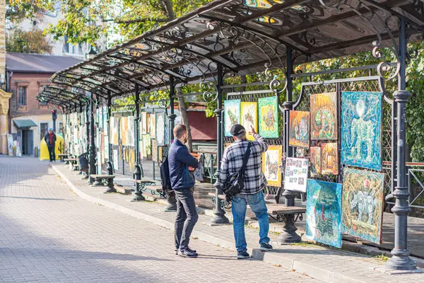 Kapalı tepe örtüsü, karmaşık siyah metal yapısı, resim tahtaları, gündüz kuşağı, günlük kıyafet, birbiriyle etkileşen iki kişi, resimler, Kyiv, Ukrayna 10-11-2024