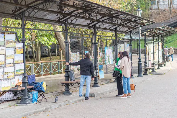Ukrayna 10-11-2024 tarihli Duri Kyiv, Ukrayna 'da bir anı yakalayan, görünür, ayakta, yürüyen, belgesel tarzı üç kişi, bulutlu bir günde açık yüzlü bir yapıyla sokak sahnesi.