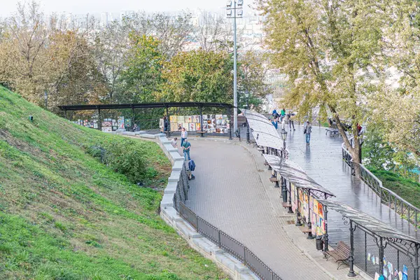 Alacakaranlıkta şehir manzarası, yemyeşil tepeler, hareketli yayalar, açık kafe, bulutlu gökyüzü, sonbahar ağaçları, binalar, çevre ışıkları Kyiv, Ukrayna 10-11-2024
