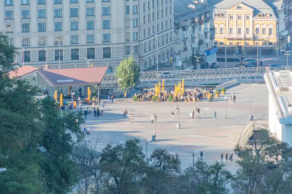 Geceleri şehir meydanı insanlarla dolup taşıyor, geleneksel-modern mimari, sıcak yapay ışıklandırma, mavi-sarı renk değişimi, kuş bakışı görüntü, şehir hayatı un Kyiv, Ukrayna 10-20-2024